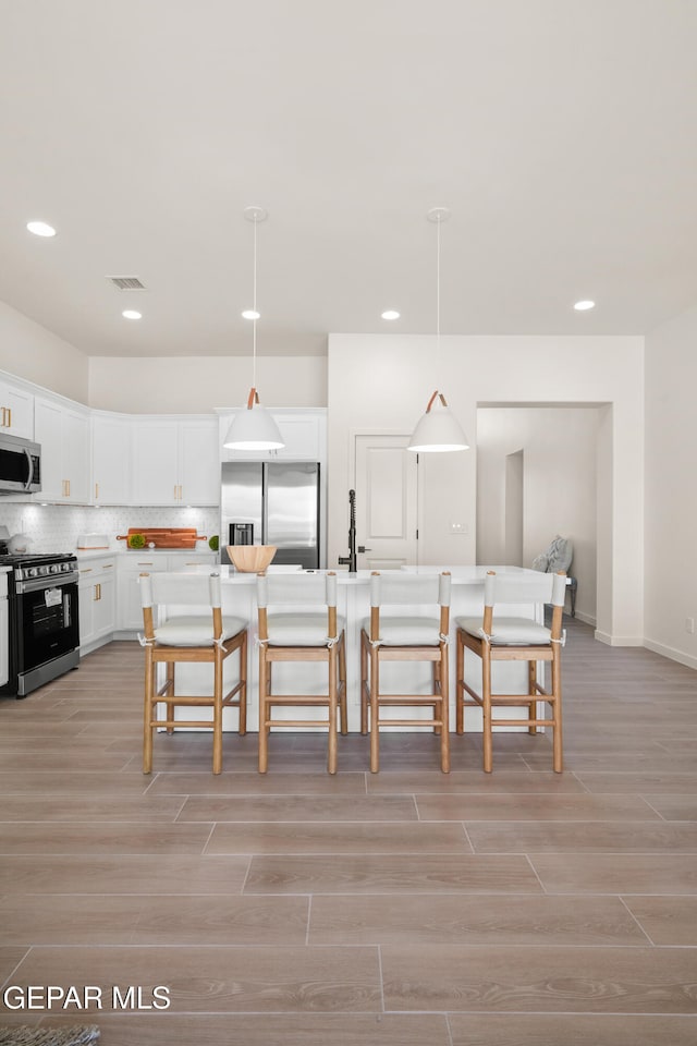 kitchen featuring an island with sink, hanging light fixtures, white cabinetry, stainless steel appliances, and a breakfast bar area