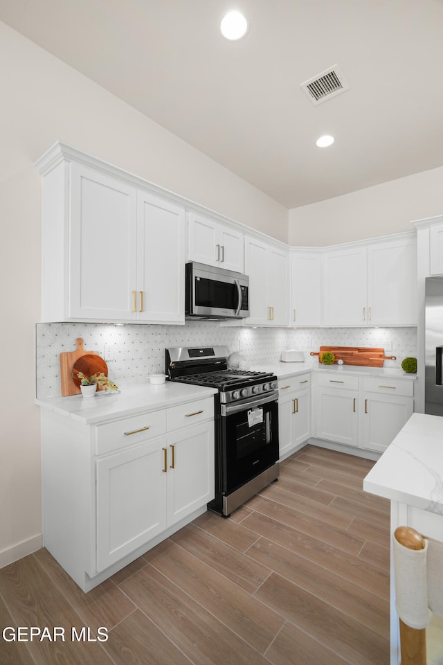 kitchen with tasteful backsplash, light stone countertops, appliances with stainless steel finishes, white cabinets, and light hardwood / wood-style flooring