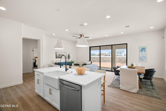 kitchen with hanging light fixtures, a center island with sink, white cabinetry, stainless steel dishwasher, and light wood-type flooring