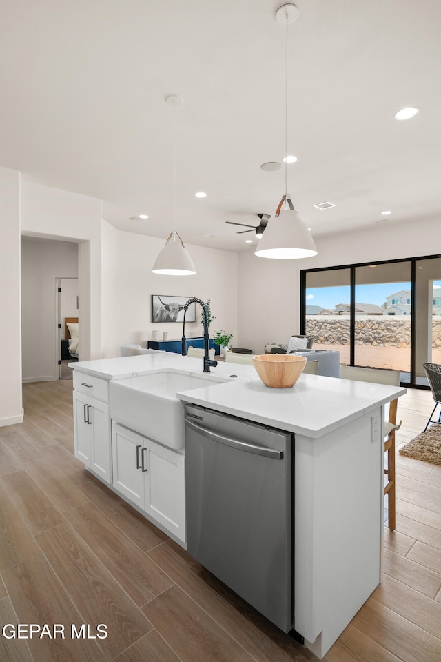 kitchen featuring dishwasher, a kitchen island with sink, light hardwood / wood-style flooring, hanging light fixtures, and white cabinets