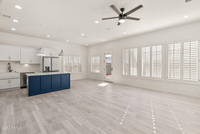 kitchen featuring white cabinets, hanging light fixtures, a kitchen island, light hardwood / wood-style floors, and stainless steel appliances