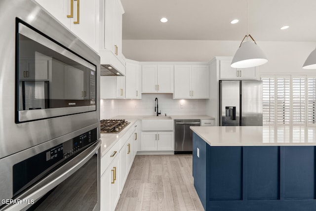 kitchen with tasteful backsplash, appliances with stainless steel finishes, light wood-type flooring, white cabinetry, and decorative light fixtures