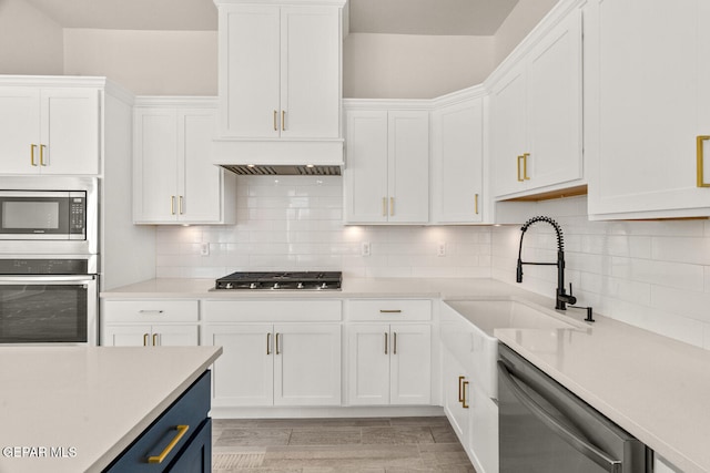 kitchen with appliances with stainless steel finishes, light wood-type flooring, blue cabinets, white cabinets, and decorative backsplash