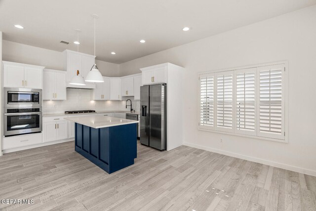 kitchen with hanging light fixtures, a kitchen island, appliances with stainless steel finishes, white cabinetry, and light wood-type flooring