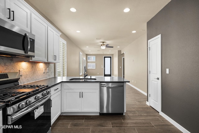 kitchen with appliances with stainless steel finishes, kitchen peninsula, white cabinets, and sink