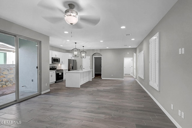 kitchen featuring appliances with stainless steel finishes, white cabinetry, wood-type flooring, decorative light fixtures, and a center island