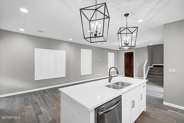 kitchen featuring white cabinets, a kitchen island with sink, stainless steel dishwasher, sink, and decorative light fixtures