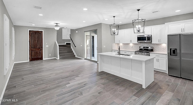 kitchen featuring a kitchen island with sink, stainless steel appliances, sink, decorative light fixtures, and white cabinets