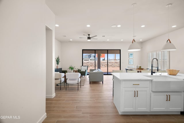 kitchen with hanging light fixtures, sink, light wood-type flooring, white cabinets, and ceiling fan