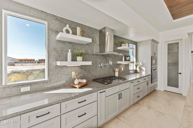 kitchen featuring light stone countertops, stainless steel appliances, wall chimney range hood, tasteful backsplash, and white cabinets