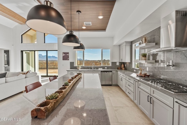 kitchen featuring stone counters, wall chimney range hood, a towering ceiling, decorative backsplash, and appliances with stainless steel finishes