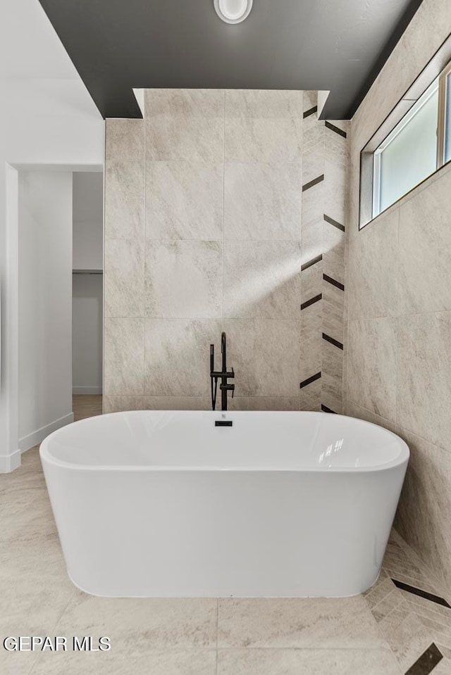 bathroom with tile patterned floors, a washtub, and tile walls