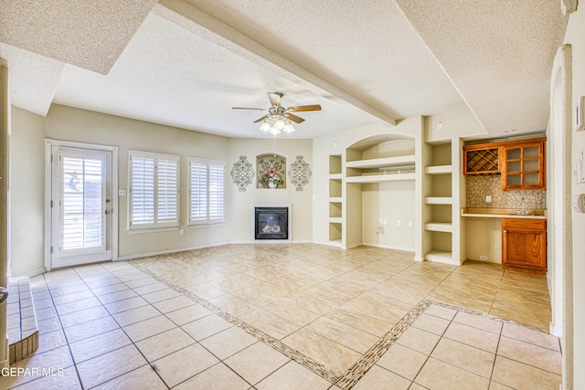 unfurnished living room with a textured ceiling, ceiling fan, built in shelves, and light tile patterned floors