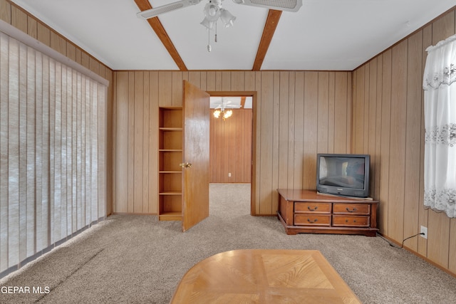 carpeted living room with beamed ceiling, wooden walls, and ceiling fan