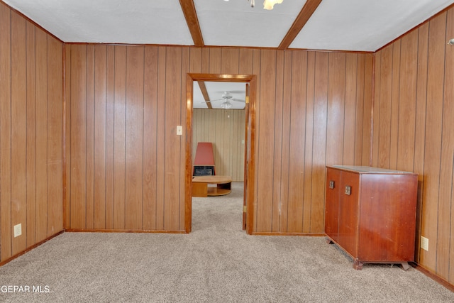 carpeted spare room with wood walls, beamed ceiling, and ceiling fan