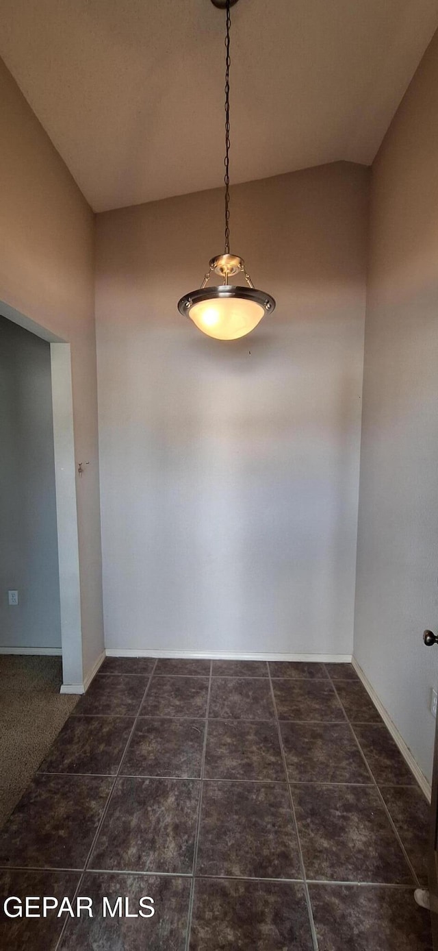 unfurnished dining area with dark tile patterned floors and lofted ceiling