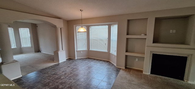 unfurnished dining area with built in features, dark colored carpet, and ornate columns