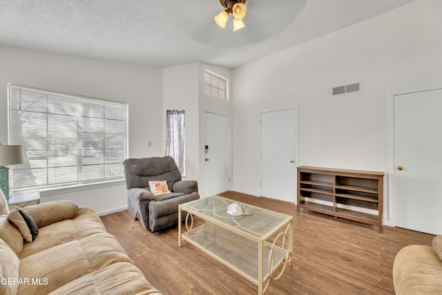 living room with a textured ceiling, ceiling fan, and light hardwood / wood-style flooring