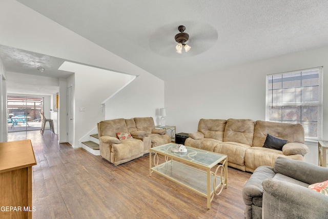 living room featuring lofted ceiling, a textured ceiling, hardwood / wood-style flooring, and ceiling fan