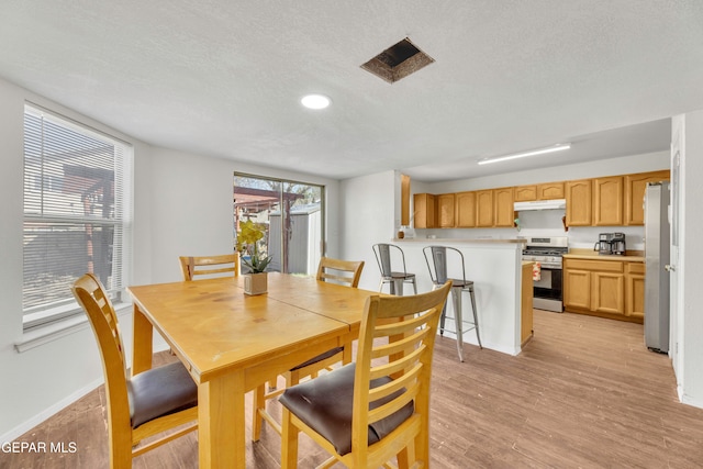 dining room with light wood-type flooring and a textured ceiling