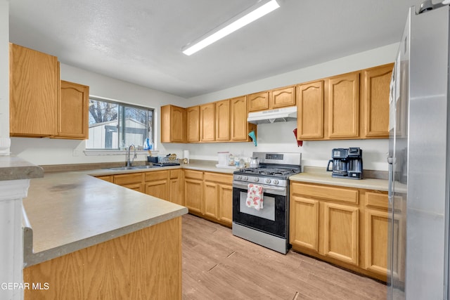 kitchen with stainless steel appliances, light brown cabinetry, sink, and light hardwood / wood-style flooring