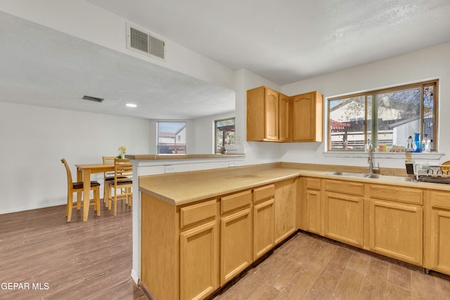 kitchen featuring light hardwood / wood-style floors, kitchen peninsula, a textured ceiling, sink, and light brown cabinetry