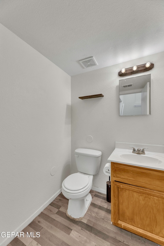 bathroom featuring wood-type flooring, vanity, toilet, and a textured ceiling