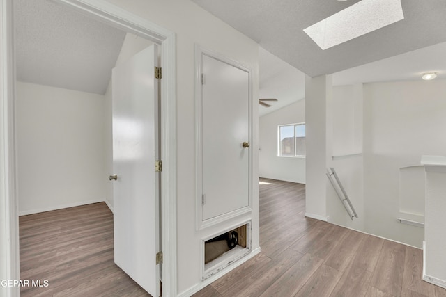 hall with lofted ceiling with skylight, hardwood / wood-style floors, and a textured ceiling