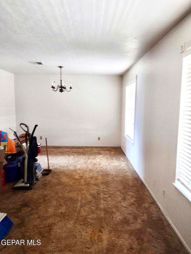 carpeted spare room featuring a chandelier and plenty of natural light