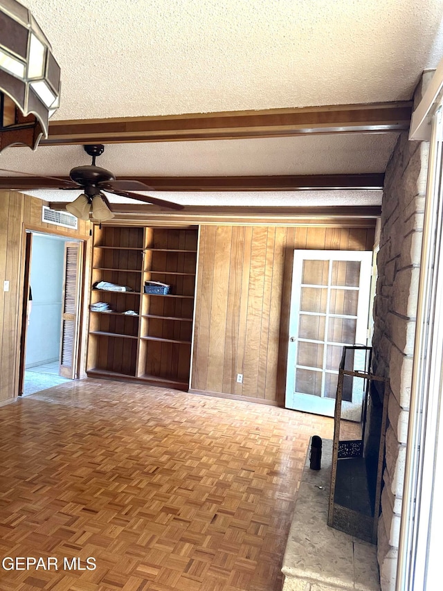 unfurnished living room with parquet flooring, wood walls, a textured ceiling, and ceiling fan