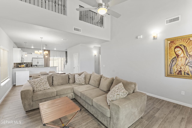 living room with a high ceiling, hardwood / wood-style flooring, and ceiling fan with notable chandelier