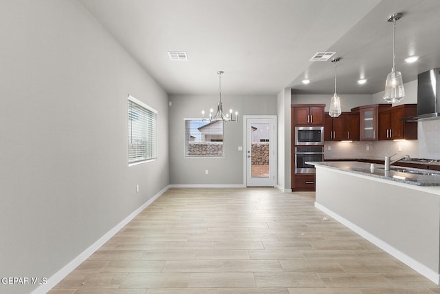 kitchen with wall chimney exhaust hood, sink, decorative light fixtures, a chandelier, and appliances with stainless steel finishes