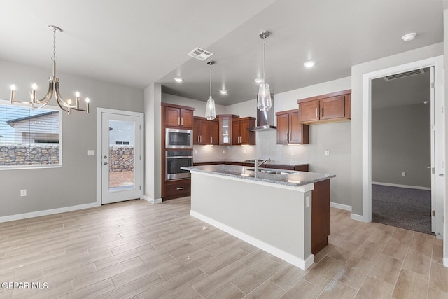 kitchen with light hardwood / wood-style flooring, stainless steel appliances, dark stone countertops, a center island with sink, and an inviting chandelier