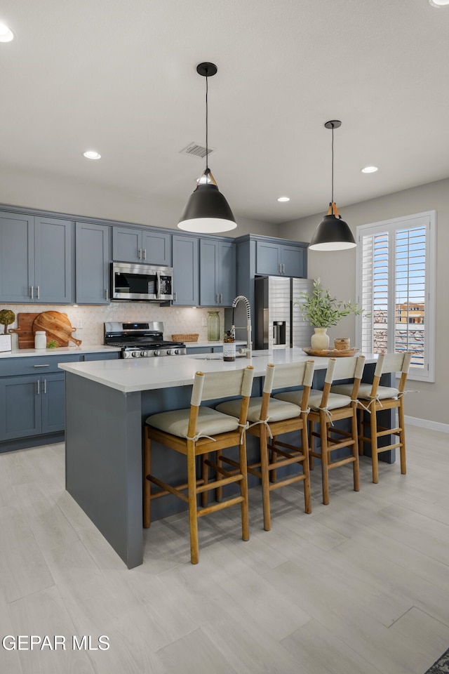 kitchen featuring appliances with stainless steel finishes, backsplash, pendant lighting, and an island with sink