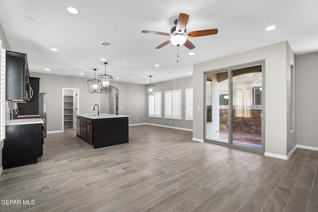 kitchen with sink, an island with sink, hanging light fixtures, and dark hardwood / wood-style flooring