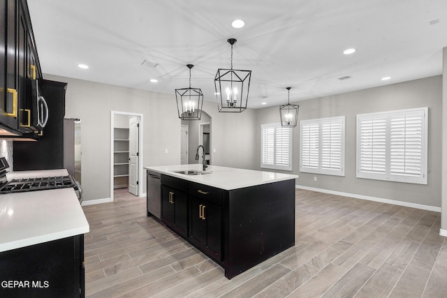 kitchen featuring hanging light fixtures, a center island with sink, sink, gas stove, and light hardwood / wood-style floors