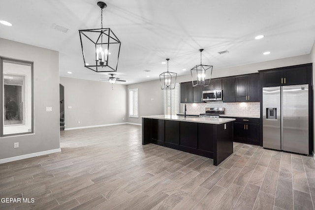 kitchen featuring a kitchen island with sink, decorative light fixtures, stainless steel appliances, and light hardwood / wood-style floors