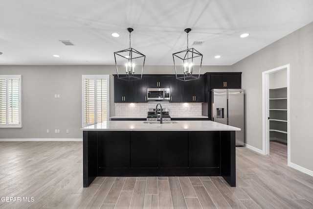 kitchen featuring appliances with stainless steel finishes, light hardwood / wood-style flooring, pendant lighting, and a center island with sink