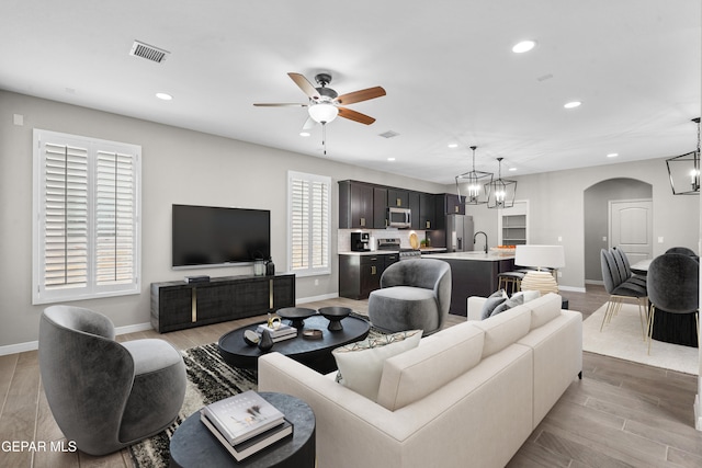 living room featuring a healthy amount of sunlight, sink, ceiling fan with notable chandelier, and light wood-type flooring