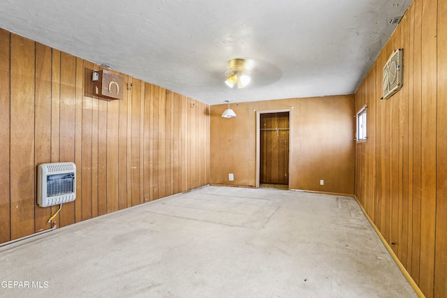 empty room featuring ceiling fan, heating unit, and wood walls