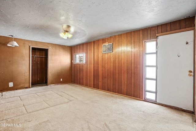 spare room featuring a wealth of natural light, wooden walls, carpet flooring, and ceiling fan