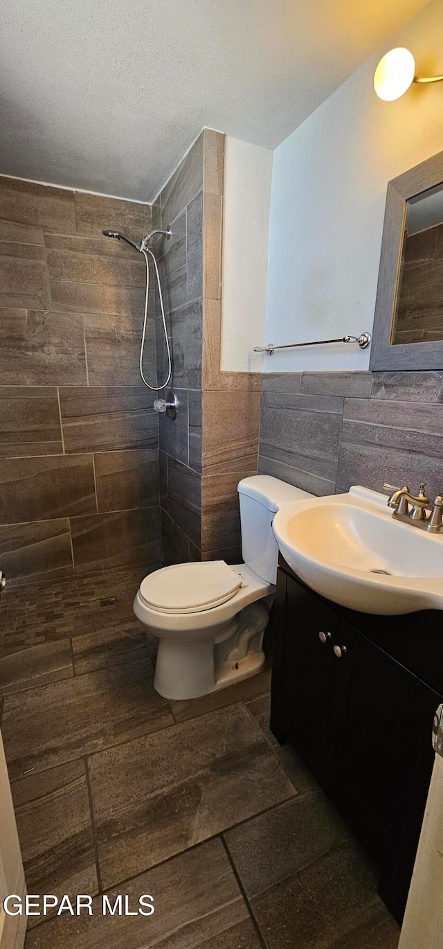 bathroom with vanity, toilet, a textured ceiling, tile walls, and a tile shower