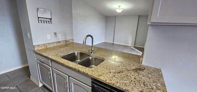 kitchen featuring light stone countertops, sink, dark tile patterned floors, and black dishwasher