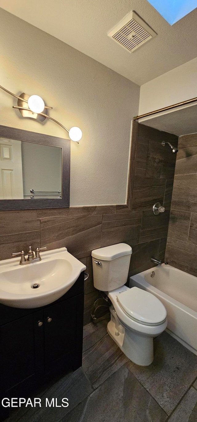 full bathroom featuring a skylight, vanity, tiled shower / bath combo, tile walls, and toilet