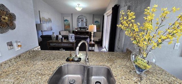 kitchen featuring open floor plan, a sink, and light stone countertops