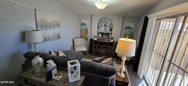 living room with a lit fireplace, vaulted ceiling, and wood finished floors