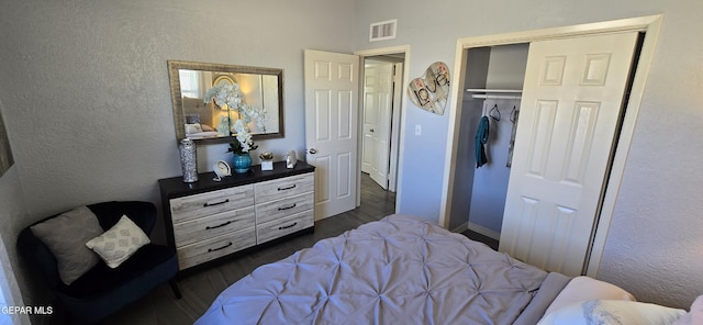 bedroom featuring baseboards, visible vents, a textured wall, dark wood-style floors, and a closet