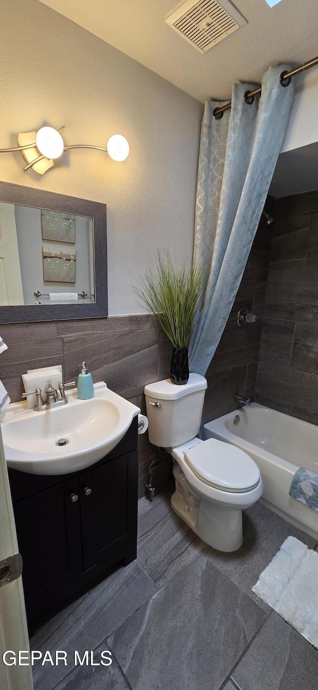 full bathroom featuring shower / bath combo, visible vents, toilet, a wainscoted wall, and vanity