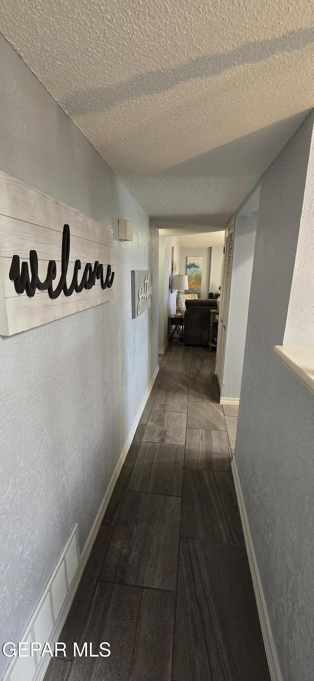 hall featuring baseboards, vaulted ceiling, a textured ceiling, and a textured wall