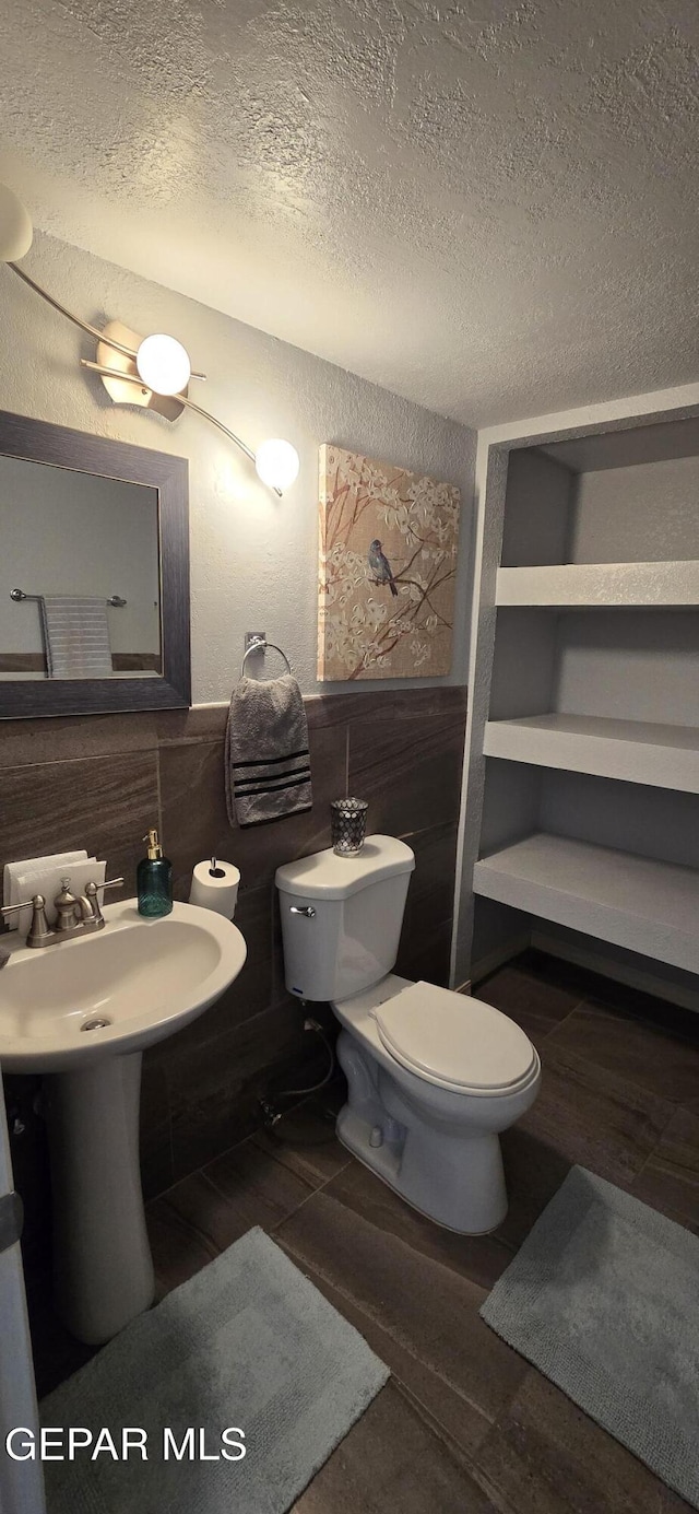 half bathroom featuring a textured wall, toilet, wainscoting, wood finished floors, and a textured ceiling